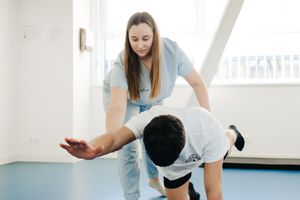A physiotherapist assists a patient in stretching exercises indoors.